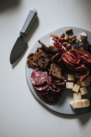 An elegant party platter showcasing rolled deli meats, olives, nuts, and artisan crackers on a rustic table.