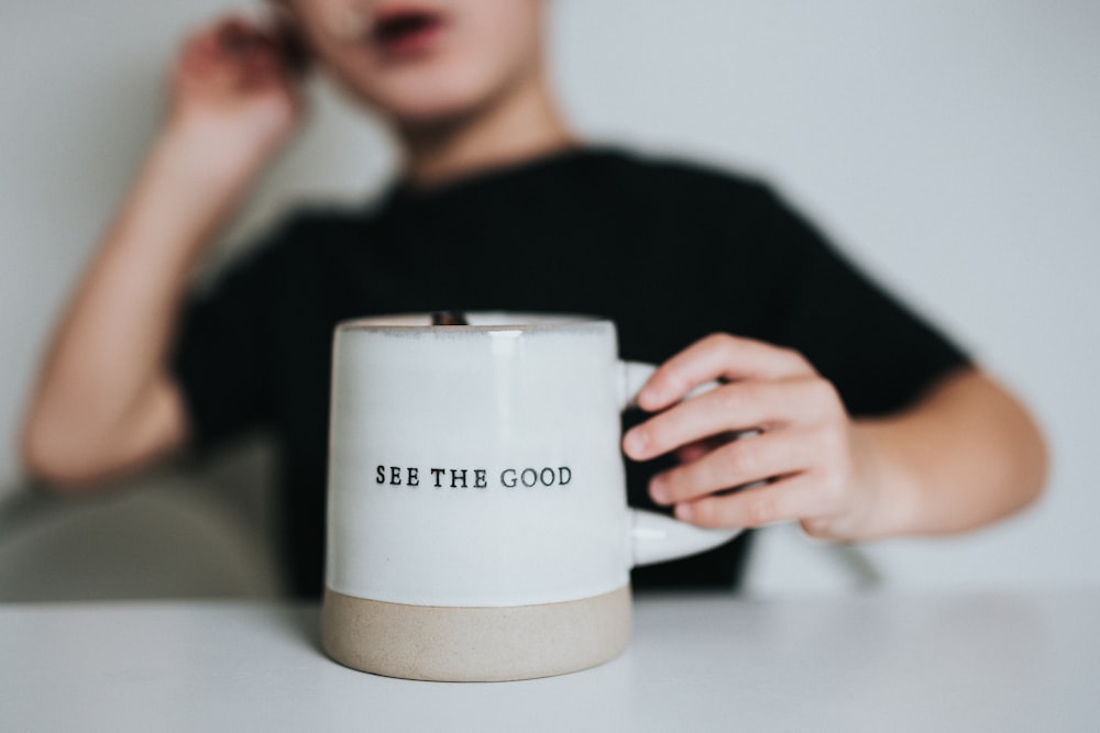 Femme en chemise noire tenant une tasse en céramique blanche