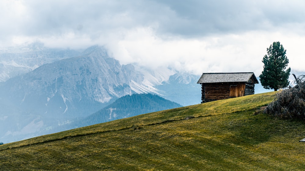 Braunes Holzhaus auf grünem Grasfeld in der Nähe eines schneebedeckten Berges tagsüber