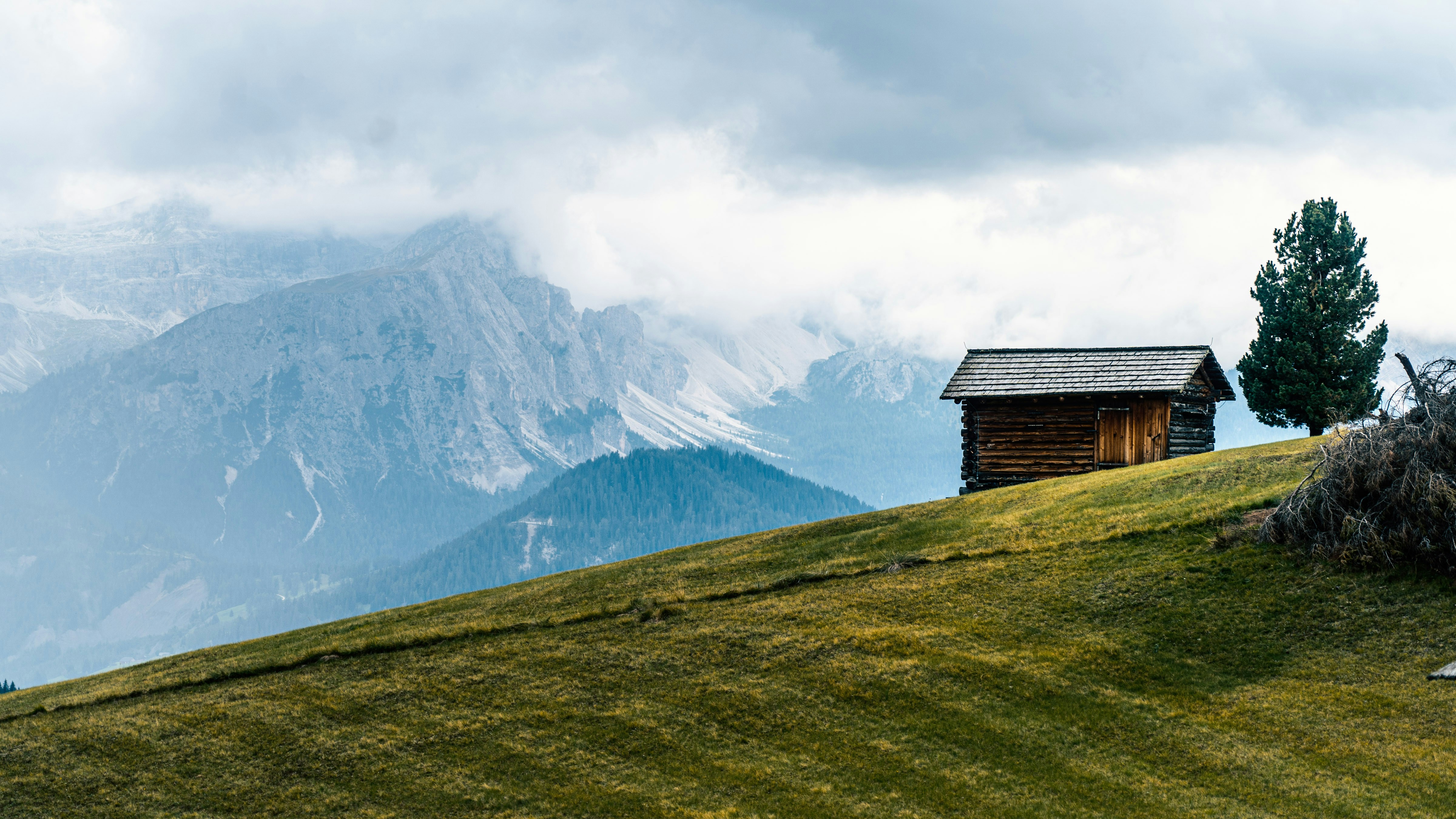 brown wooden house on green grass field near snow covered mountain during daytime