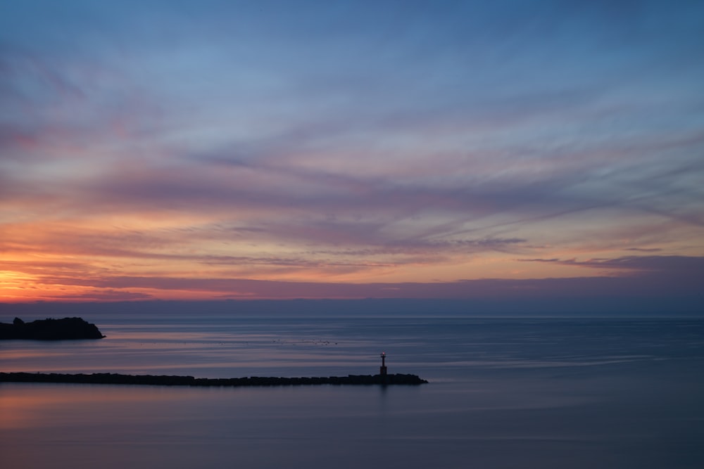 silhouette of person standing on sea dock during sunset