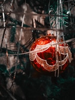 Close-up of a sparkling red and gold Christmas ornament hanging on a pine tree.