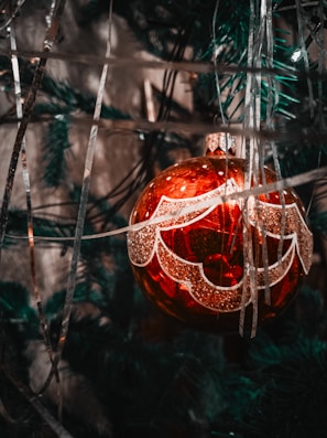 Close-up of a sparkling red and gold Christmas ornament hanging on a pine tree.