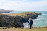 A couple standing on a cliff, gazing at the ocean.