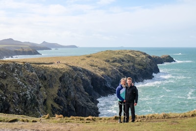 A couple standing on a cliff, gazing at the ocean.