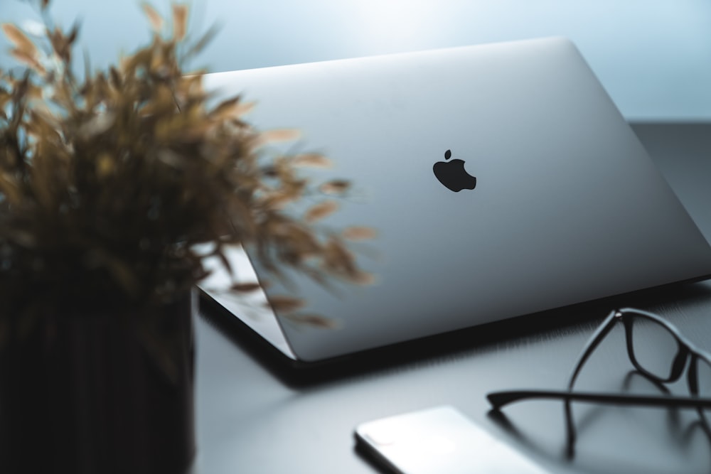 silver macbook beside black framed eyeglasses