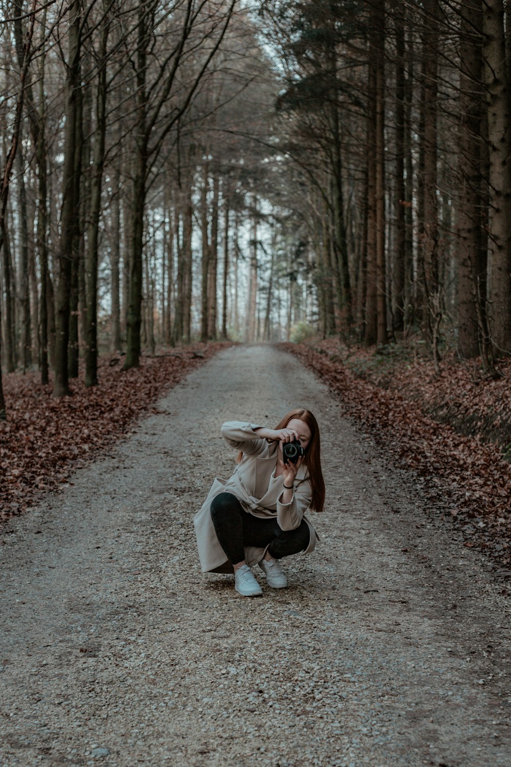 woman in white coat sitting on pathway surrounded by trees during daytime