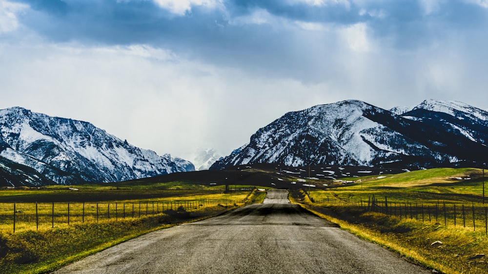 gray concrete road near green grass field and snow covered mountain during daytime