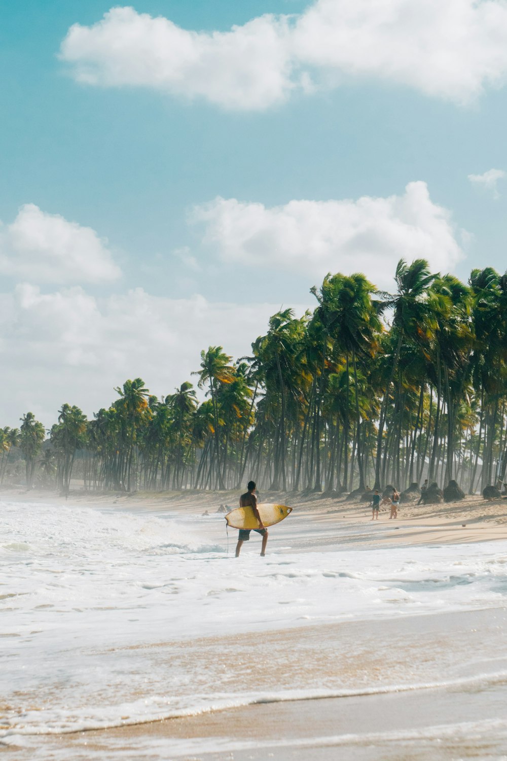 personne en chemise jaune portant une planche de surf marron marchant sur la plage pendant la journée