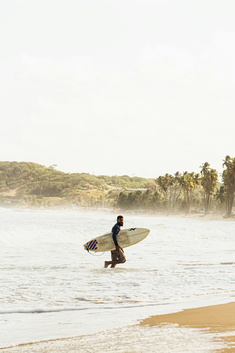 man in black and white long sleeve shirt holding white surfboard on beach during daytime