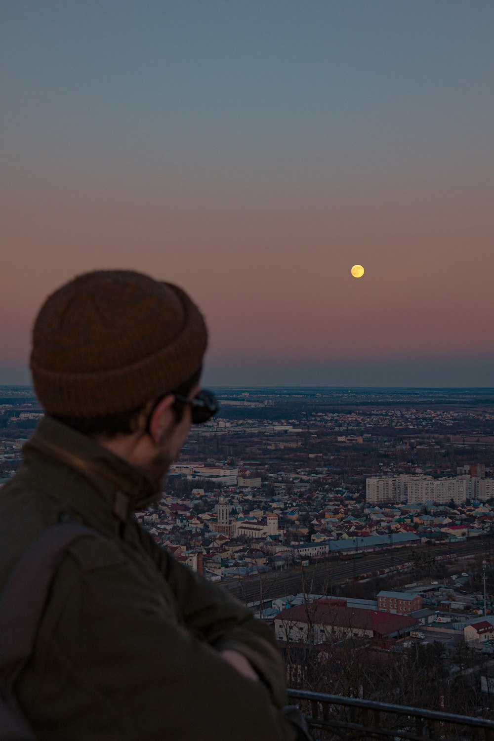 man in brown jacket and black cap looking at city buildings during daytime