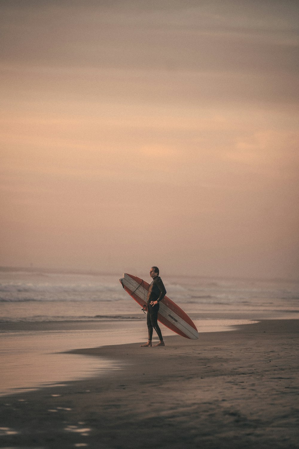 man in red shirt holding red surfboard walking on beach during daytime