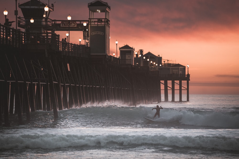 man surfing on sea waves near building during night time