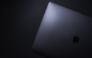 A sleek, closed laptop with a metallic finish seen from an angled overhead perspective, resting on a dark surface. The logo on the laptop is clearly visible.