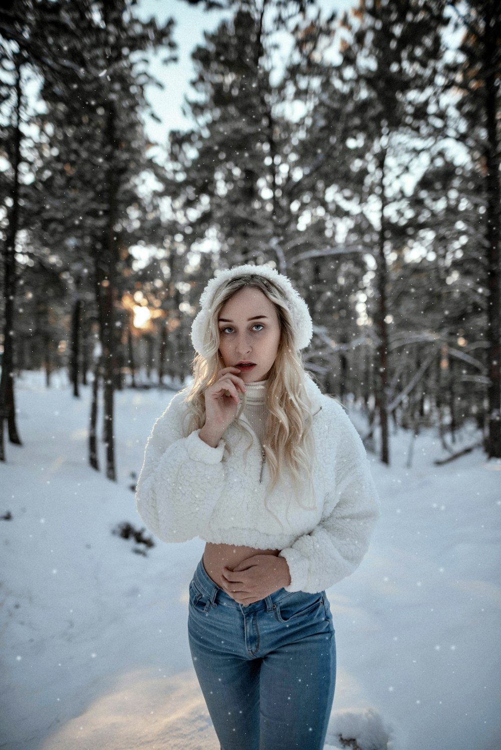 mulher no suéter branco e jeans azuis em pé no chão coberto de neve durante o dia