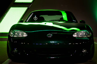 A sleek black vehicle illuminated by neon green lights, parked outside a modern workshop glowing softly in the dark.