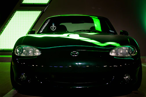 A sleek black vehicle illuminated by neon green lights, parked outside a modern workshop glowing softly in the dark.