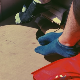 Several sock-covered feet rest on a beige surface, with natural light casting shadows. A red object with visible text is partially visible in the foreground.