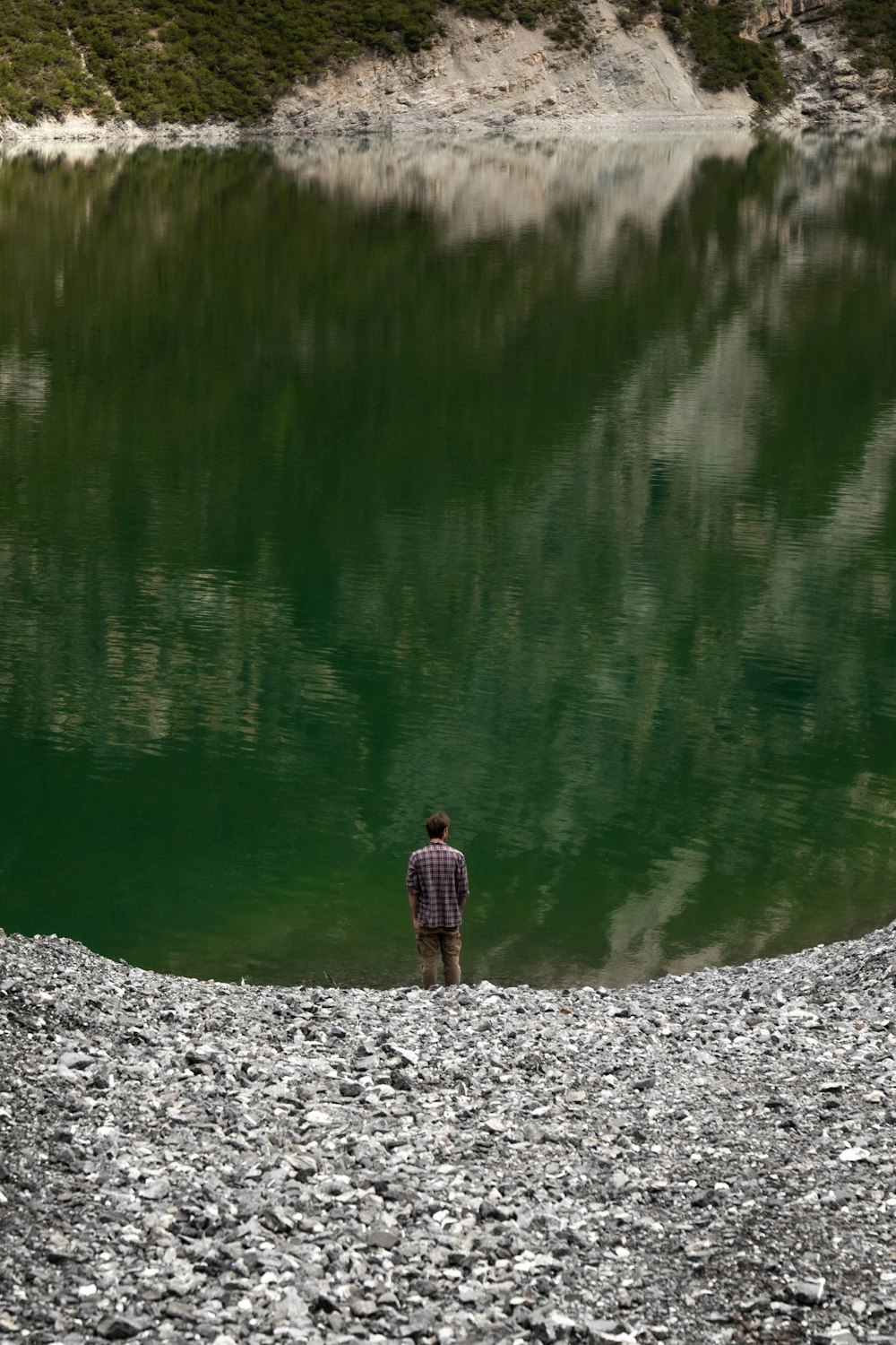 Hombre en chaqueta marrón de pie en el suelo rocoso cerca del lago durante el día