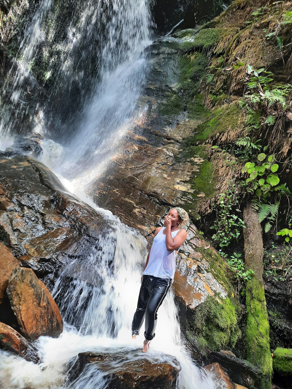 woman in black tank top and black pants standing on rock near waterfalls during daytime