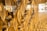 A close-up view of an artistic wall installation featuring an array of geometric, hourglass-shaped glass elements. These elements capture and reflect light, creating a golden, shimmering effect across the surface.