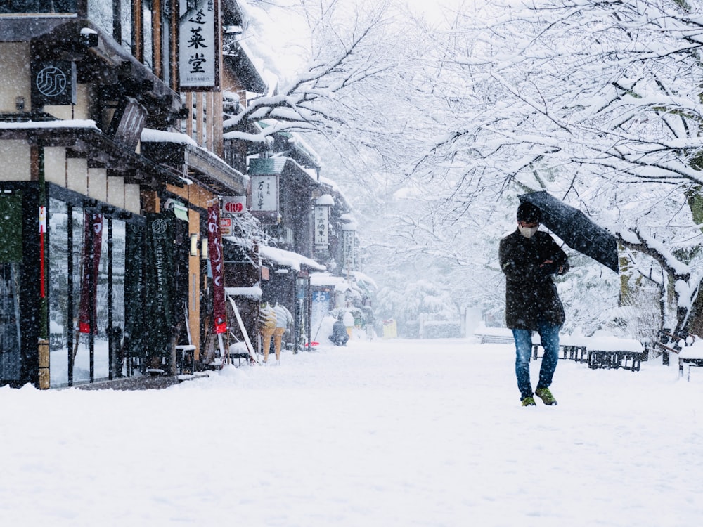 man in black jacket and blue denim jeans walking on snow covered ground during daytime