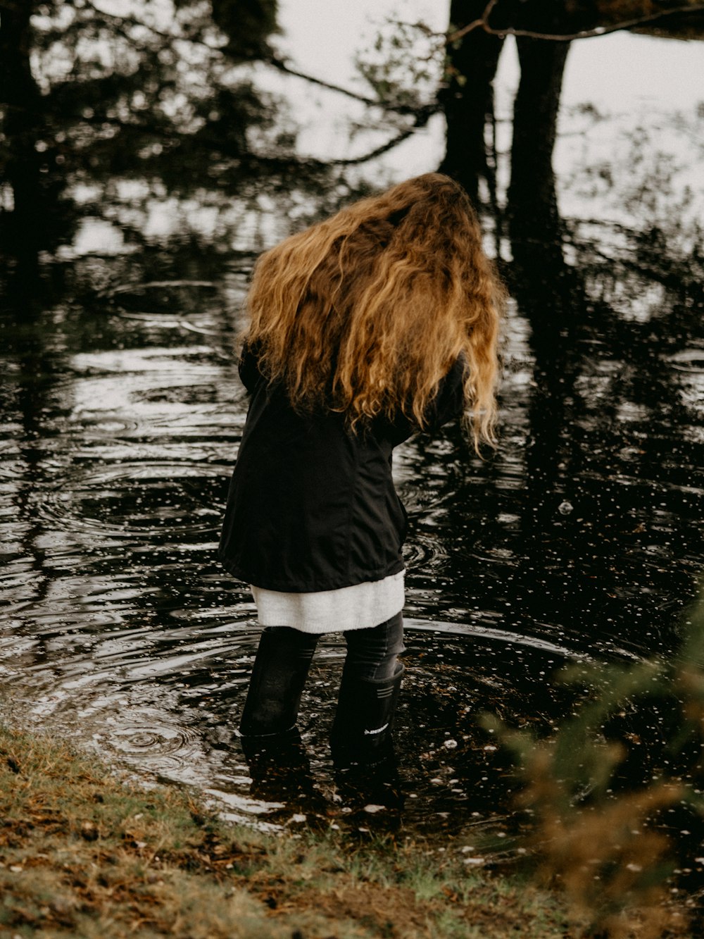 Mujer con chaqueta negra y pantalones blancos de pie sobre el agua