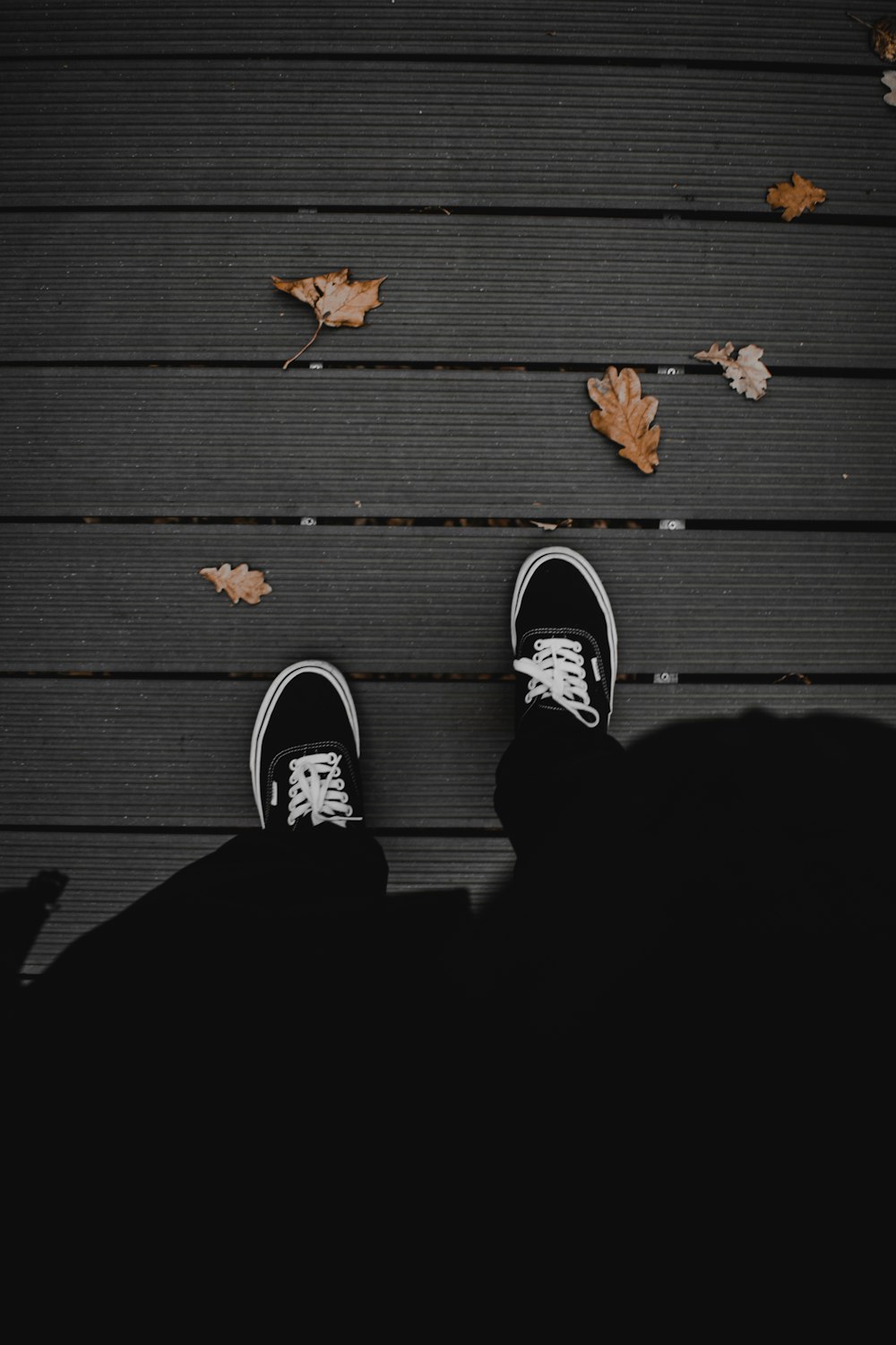 Persona con pantalones negros con zapatillas blancas y negras de pie sobre el piso de madera negro