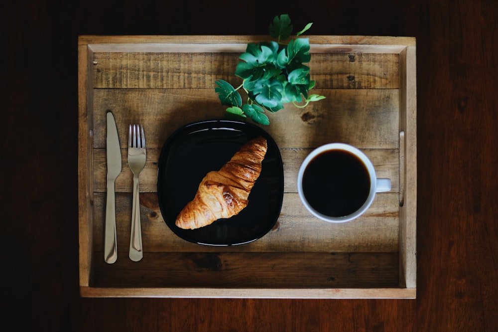 white ceramic mug beside stainless steel fork and bread knife on brown wooden chopping board