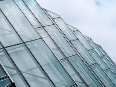 Rows of glass panels form a series of modern architectural structures, with a focus on their sleek, angular design. The panels are transparent and reflect the light, giving a sense of openness and space against a backdrop of a partly cloudy sky.