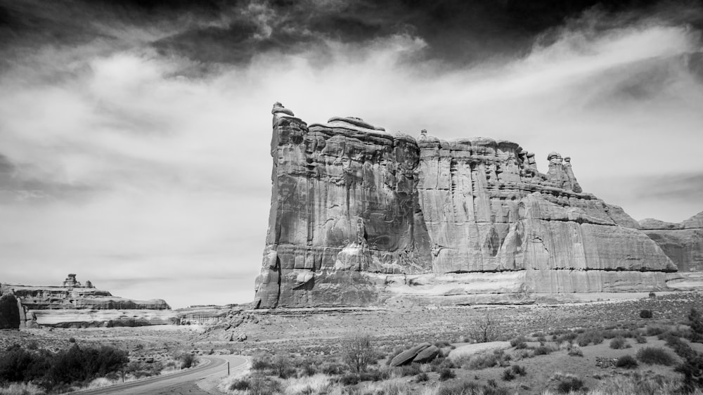 grayscale photo of rock formation under cloudy sky