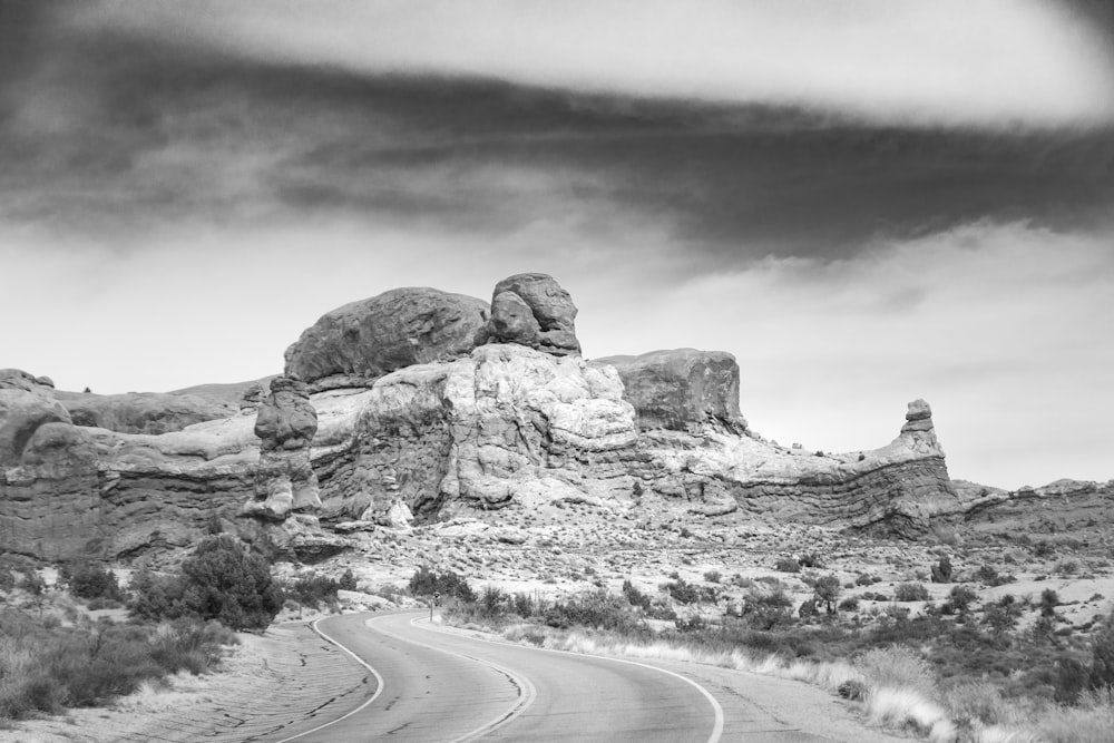 grayscale photo of road near rock formation