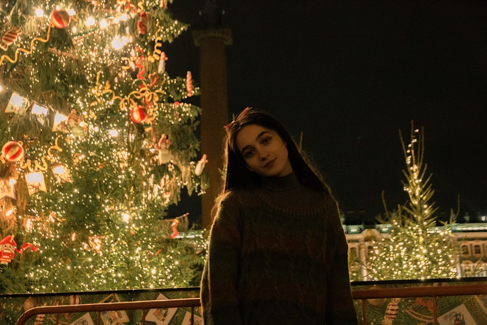 Mujer en suéter marrón de pie cerca del árbol de Navidad verde