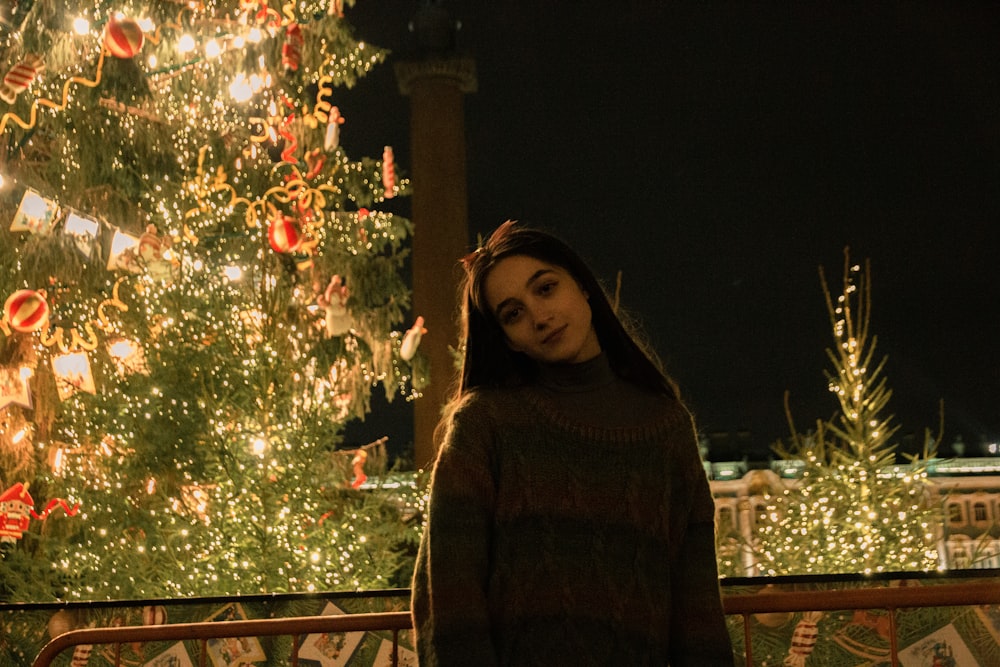 Femme en pull marron debout près de l’arbre de Noël vert