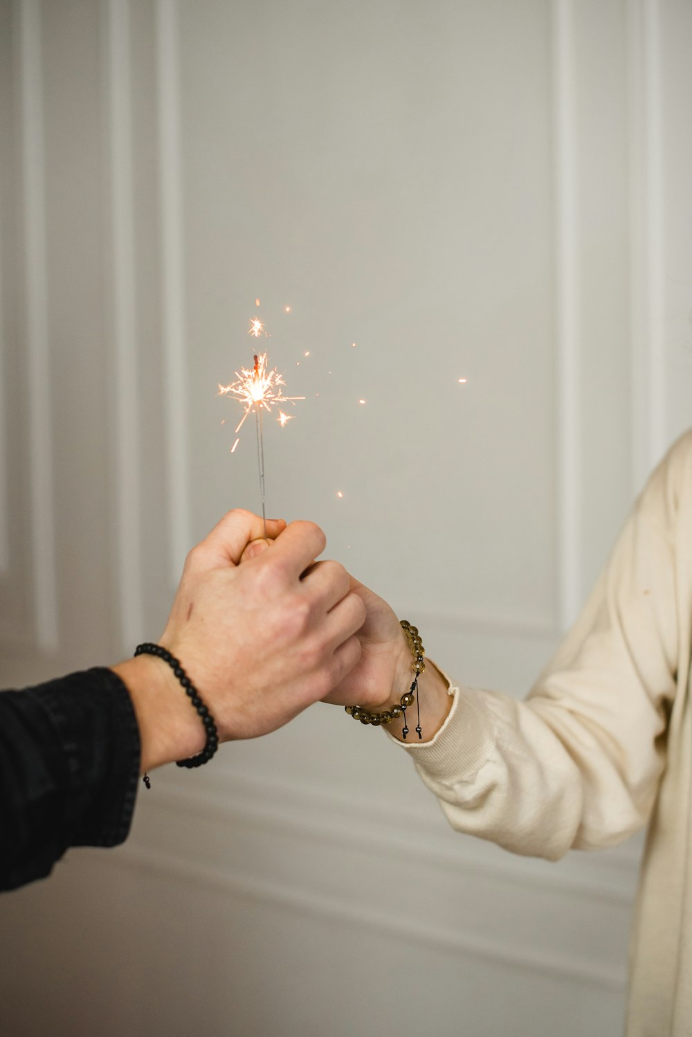 person holding lighted sparkler in front of white curtain