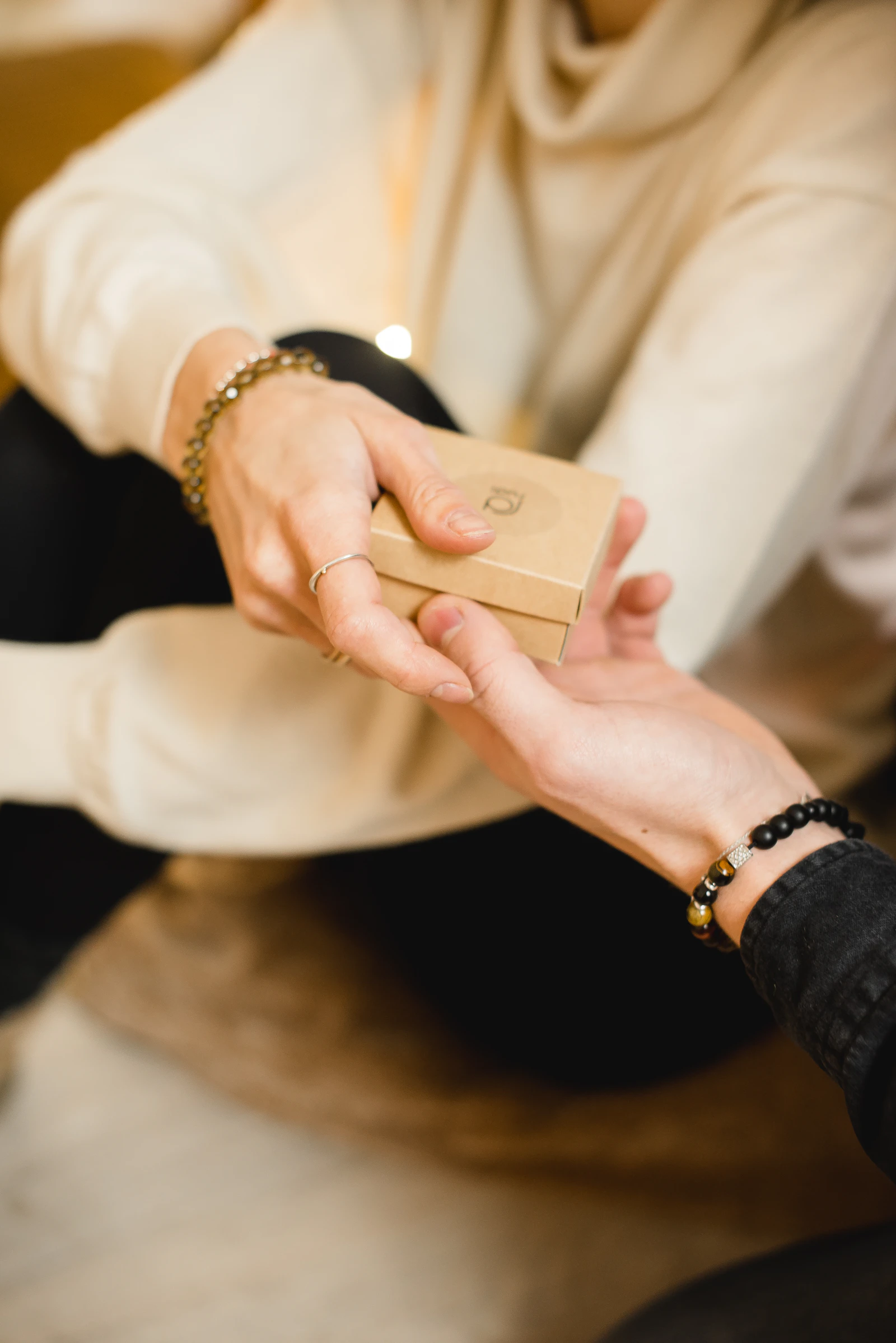 A small kraft gift box passing from one pair of hands to another