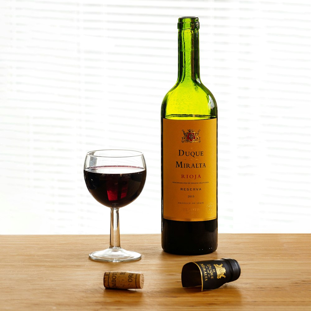 garrafa de vidro verde ao lado do copo de vinho transparente na mesa de madeira marrom
