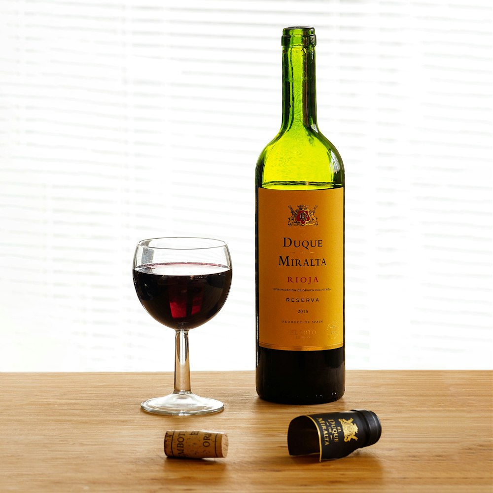 green glass bottle beside clear wine glass on brown wooden table