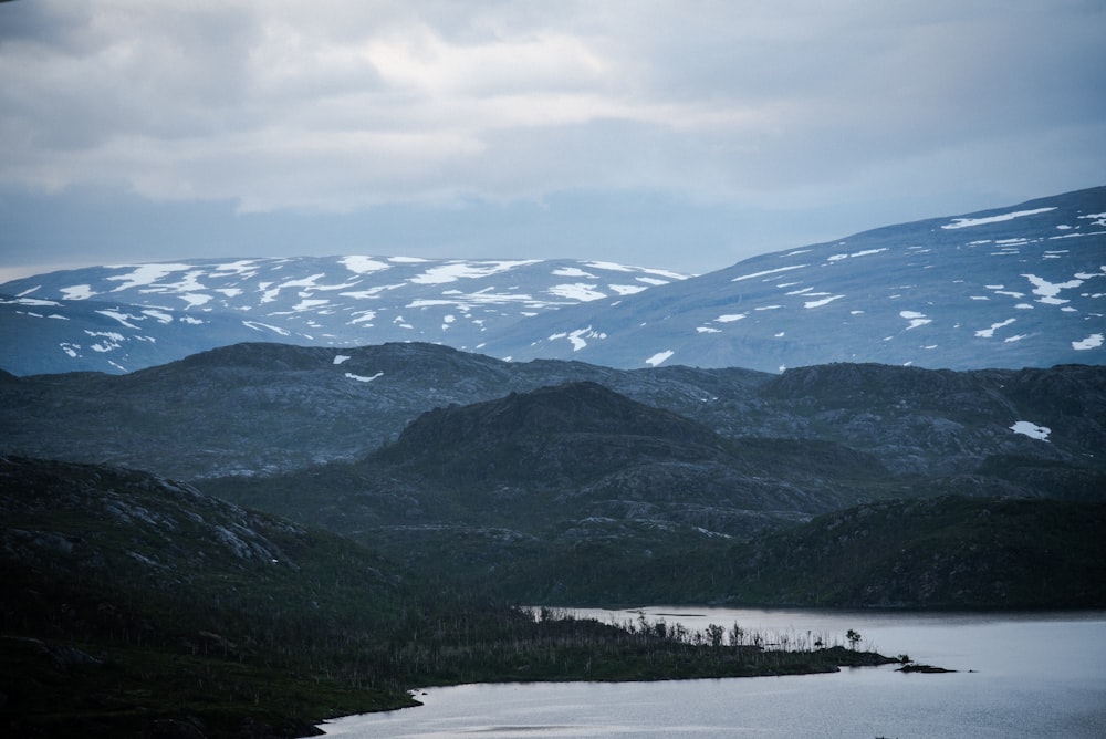 snow covered mountain near lake under white clouds during daytime