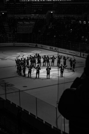 A black and white photo of a hockey team raising their sticks to salute the crowd after a game
