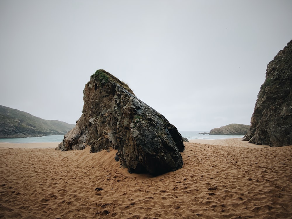 brown rock formation on brown sand near body of water during daytime