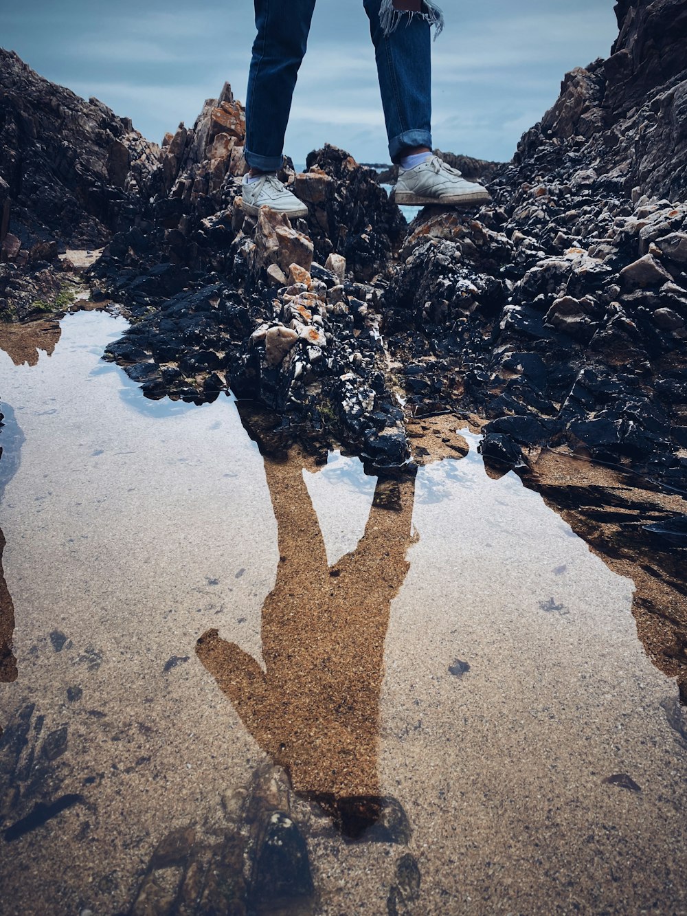 person standing on gray sand near body of water during daytime