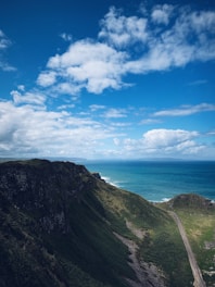 A scenic coastal road winding through cliffs under a bright blue sky.