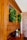A wooden cabinet with glass doors adorned with lush green wreaths. Several small decorative objects, including wooden pepper mills and small potted plants, sit on the cabinet surface. The cabinet is set against a background featuring a light-colored brick wall.