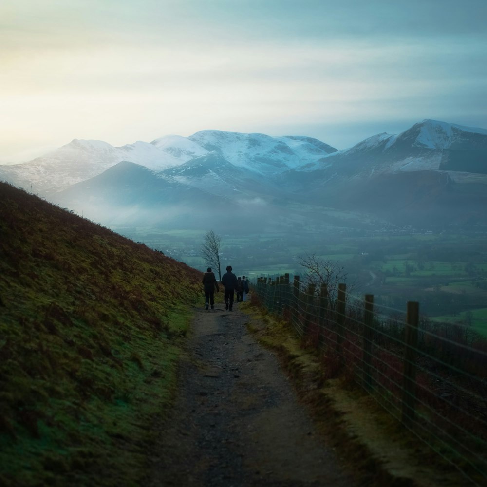 person walking on pathway near green grass field and mountains during daytime