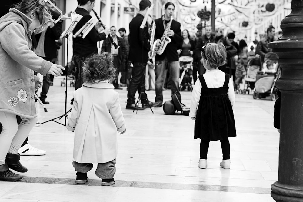 grayscale photo of girl in white coat standing on floor