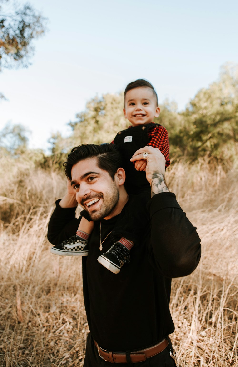 man in black jacket carrying baby in red and white checkered shirt during daytime