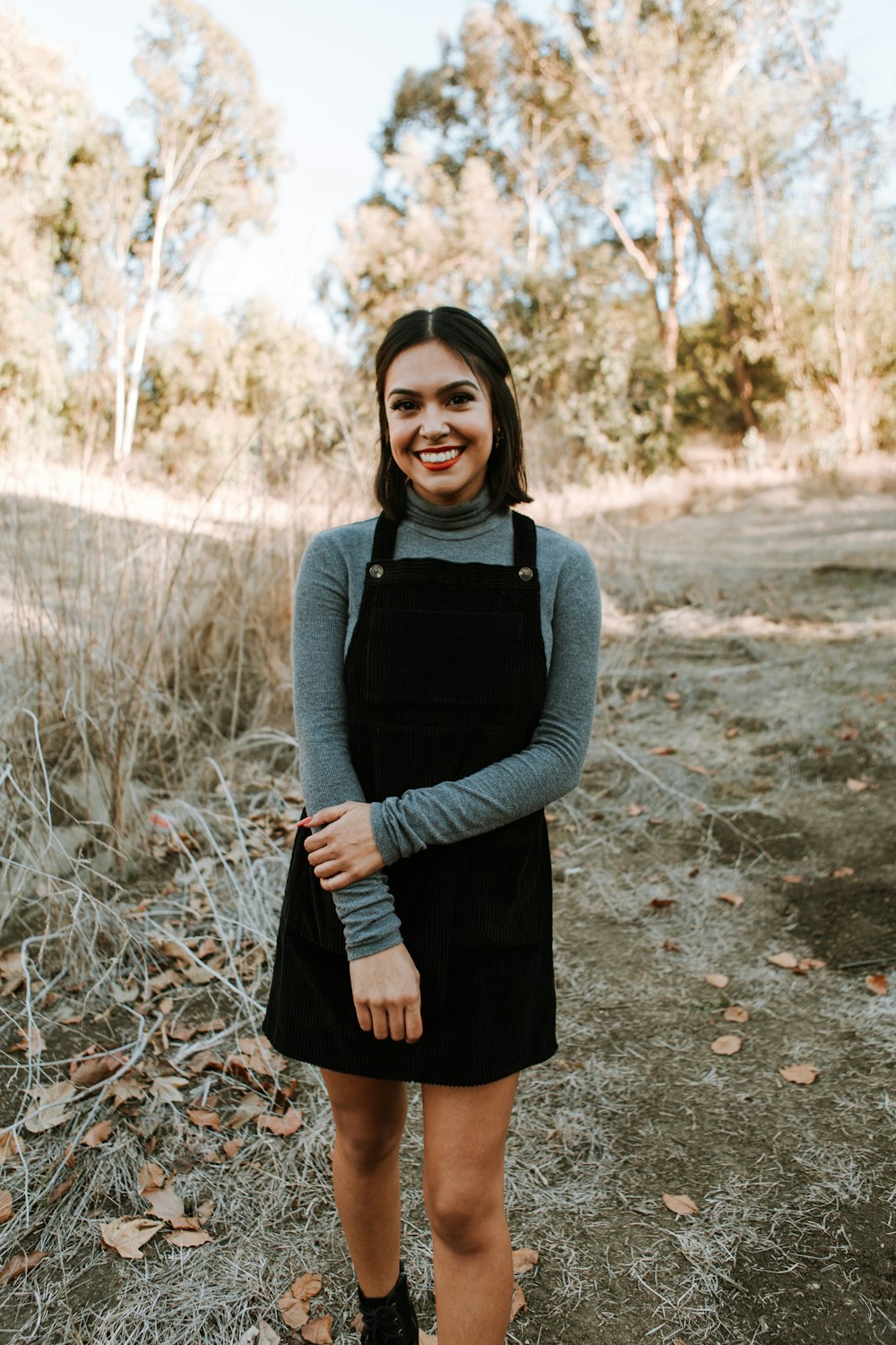 woman in gray long sleeve shirt and black skirt standing on brown dried leaves during daytime