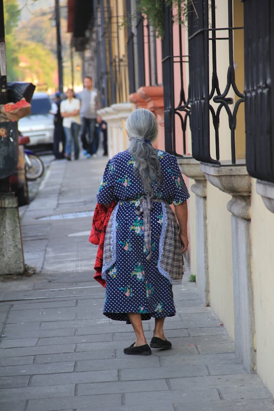 woman in red and black dress walking on sidewalk during daytime in Antigua Guatemala Guatemala