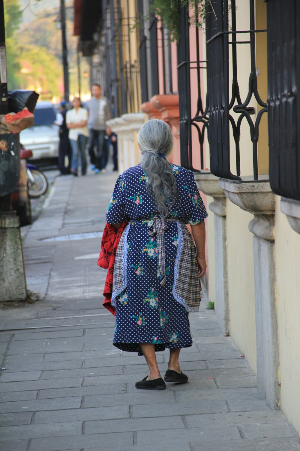 Frau in rotem und schwarzem Kleid, die tagsüber auf dem Bürgersteig spazieren geht